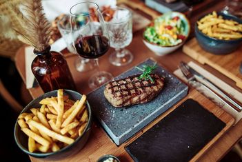 Gegrilltes Steak mit Pommes, Salat und Rotwein auf einem Holztisch. slide-5