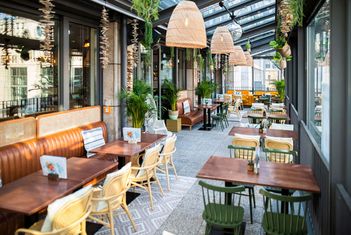 Straßencafé mit Pflanzen, Holztischen und Rattanstühlen. slide-9